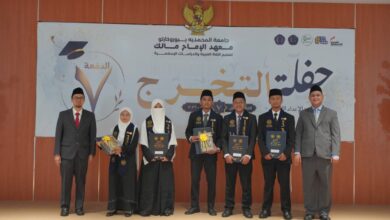 Para wisudawan dan pimpinan institusi berpose bersama di atas panggung dengan latar belakang banner bertuliskan bahasa Arab dan logo wisuda.