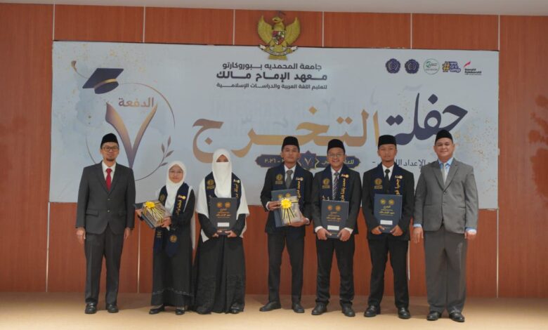 Para wisudawan dan pimpinan institusi berpose bersama di atas panggung dengan latar belakang banner bertuliskan bahasa Arab dan logo wisuda.