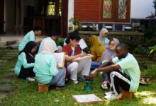 Sejumlah mahasiswa mengenakan kaos seragam hijau toska asyik belajar dan mempraktikkan proses membatik di atas rumput taman bersama peserta asing.