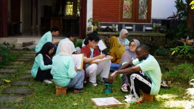 Sejumlah mahasiswa mengenakan kaos seragam hijau toska asyik belajar dan mempraktikkan proses membatik di atas rumput taman bersama peserta asing.