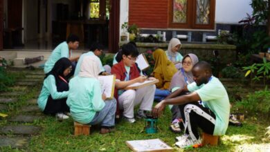 Sejumlah mahasiswa mengenakan kaos seragam hijau toska asyik belajar dan mempraktikkan proses membatik di atas rumput taman bersama peserta asing.