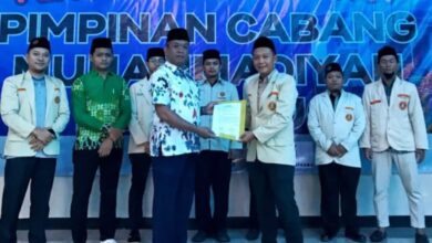 Tangan seorang peserta memegang canting dan menorehkan cairan malam di atas kain putih bermotif batik di dalam ruangan.