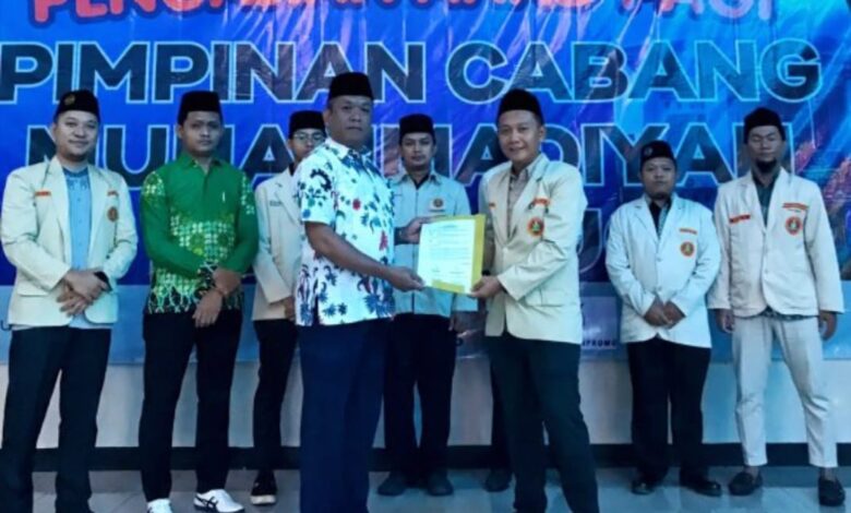Tangan seorang peserta memegang canting dan menorehkan cairan malam di atas kain putih bermotif batik di dalam ruangan.