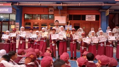 Sejumlah siswa berseragam merah putih berdiri berjejer sambil memegang piala, medali, dan sertifikat prestasi di halaman sekolah.
