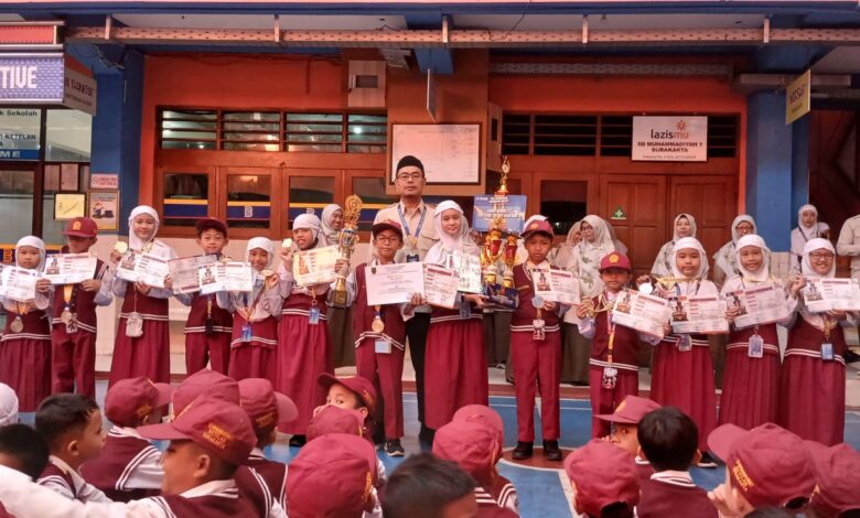 Sejumlah siswa berseragam merah putih berdiri berjejer sambil memegang piala, medali, dan sertifikat prestasi di halaman sekolah.