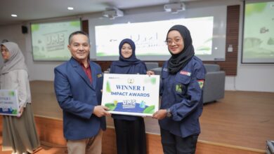 Seorang pria mengenakan jas blazer biru menyerahkan plakat penghargaan bertuliskan Winner 1 Impact Awards kepada mahasiswi berhijab di atas panggung.