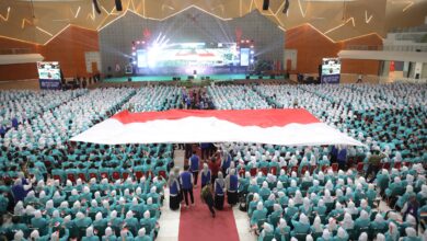 Ribuan mahasiswa baru duduk memenuhi ruang auditorium besar sambil membentangkan bendera merah putih raksasa di bagian tengah.