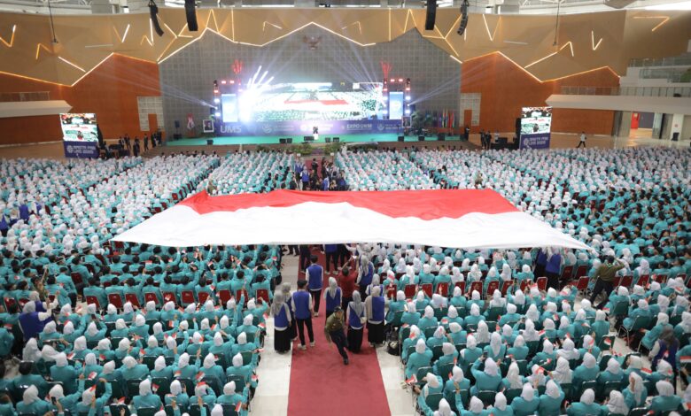 Ribuan mahasiswa baru duduk memenuhi ruang auditorium besar sambil membentangkan bendera merah putih raksasa di bagian tengah.