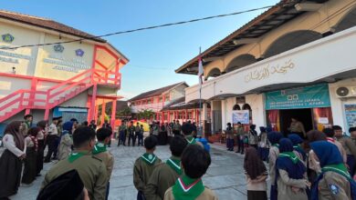 Sekelompok siswa pramuka SMP Muhammadiyah Jepara sedang melaksanakan upacara pembukaan atau penutupan kegiatan Kemah Taaruf di halaman sekolah pada pagi hari yang cerah, dikelilingi gedung sekolah dan masjid.