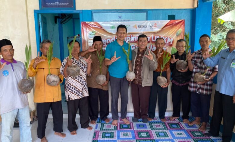Sembilan pria berpose bersama sambil memamerkan bibit kelapa kopyor yang telah bertunas di depan banner program UMKM.
