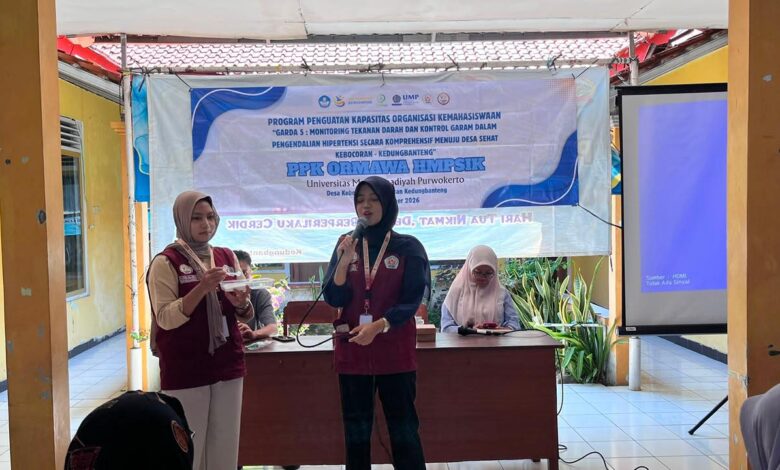 Dua mahasiswi memberikan penyuluhan kesehatan di depan banner PPK Ormawa HMPSIK Universitas Muhammadiyah Purwokerto di balai desa.