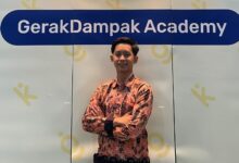 Abi Umaroh, mahasiswa Magister Ilmu Hukum UMS, berdiri mengenakan kemeja batik lengan panjang di depan spanduk GerakDampak Academy.