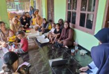 Ibu-ibu dan balita di Posyandu Krajan Sukoharjo mendengarkan penyuluhan mahasiswa fisioterapi UMS tentang bahaya posisi duduk W pada anak, menggunakan laptop di teras rumah.