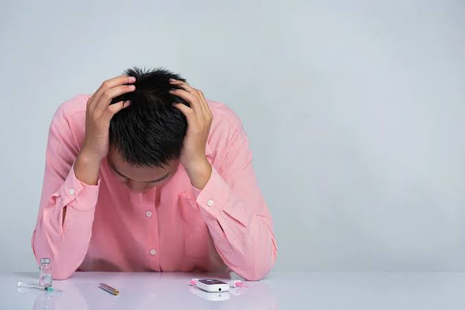 Pria tampak stres memegang kepala di meja berisi alat cek gula darah dan insulin