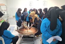 Tim pengabdian UMS mendampingi anggota KWT Sumber Rejeki menyaring cairan herbal dalam wajan besar untuk pembuatan produk olahan rempah Boyolali.