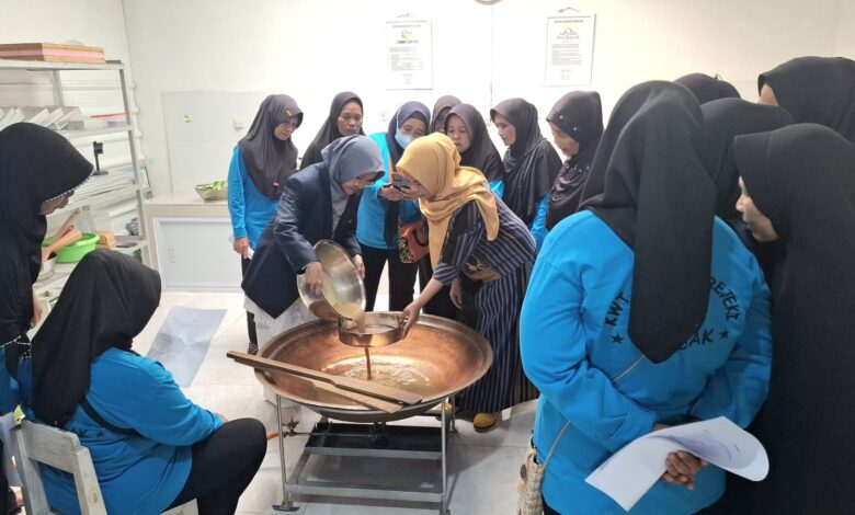 Tim pengabdian UMS mendampingi anggota KWT Sumber Rejeki menyaring cairan herbal dalam wajan besar untuk pembuatan produk olahan rempah Boyolali.