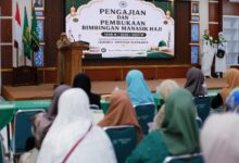 Suasana pembukaan manasik haji 2027 KBIHU Aisyiyah Surakarta, seorang pembicara wanita di podium menghadap peserta di aula.