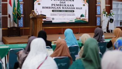 Suasana pembukaan manasik haji 2027 KBIHU Aisyiyah Surakarta, seorang pembicara wanita di podium menghadap peserta di aula.