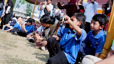 Murid SD Muhammadiyah PK Solo berkaos biru sedang membidikkan kamera saat praktik liputan Hari Anak Nasional 2026 di Taman Lingkar Lokananta.
