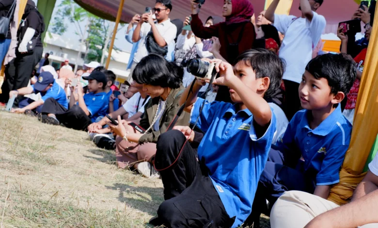 Murid SD Muhammadiyah PK Solo berkaos biru sedang membidikkan kamera saat praktik liputan Hari Anak Nasional 2026 di Taman Lingkar Lokananta.
