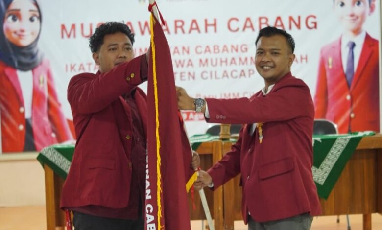 Dua pria berjas almamater merah sedang melakukan prosesi serah terima bendera pataka IMM dalam acara Musyawarah Cabang IMM Cilacap.