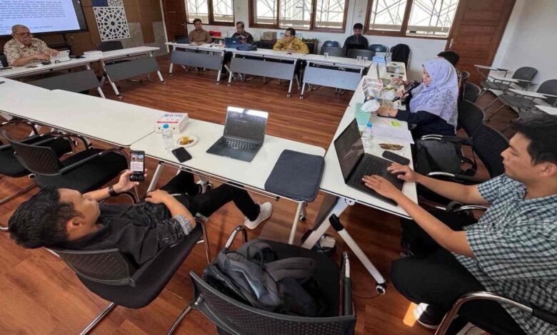 Suasana rapat revisi kurikulum PTI UMS bersama dosen dan staf di ruang rapat dengan lantai kayu. Tampak layar monitor menampilkan dokumen akademik dan beberapa peserta menggunakan laptop serta smartphone.