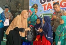 Seorang akademisi wanita berhijab menyerahkan bantuan tas ransel hitam kepada siswi SD didampingi anggota kepolisian dalam acara Kolaborasi FHIP UMS dan Polres Karanganyar.