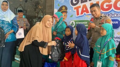 Seorang akademisi wanita berhijab menyerahkan bantuan tas ransel hitam kepada siswi SD didampingi anggota kepolisian dalam acara Kolaborasi FHIP UMS dan Polres Karanganyar.