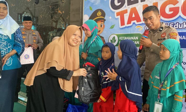 Seorang akademisi wanita berhijab menyerahkan bantuan tas ransel hitam kepada siswi SD didampingi anggota kepolisian dalam acara Kolaborasi FHIP UMS dan Polres Karanganyar.