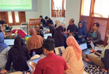 Foto kolaboratif peserta Eksekutif Camp PWM Jateng duduk lesehan menggunakan laptop, melihat layar proyektor spreadsheet KPI untuk perumusan SOP dan KPI Semester II berbasis outcome dalam rangka mencapai target PWM Jateng 2026 yang modern.