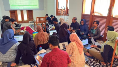 Foto kolaboratif peserta Eksekutif Camp PWM Jateng duduk lesehan menggunakan laptop, melihat layar proyektor spreadsheet KPI untuk perumusan SOP dan KPI Semester II berbasis outcome dalam rangka mencapai target PWM Jateng 2026 yang modern.