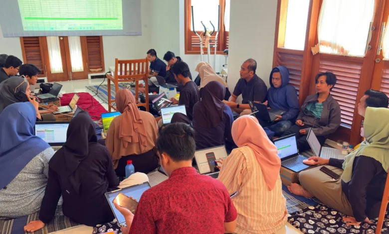 Foto kolaboratif peserta Eksekutif Camp PWM Jateng duduk lesehan menggunakan laptop, melihat layar proyektor spreadsheet KPI untuk perumusan SOP dan KPI Semester II berbasis outcome dalam rangka mencapai target PWM Jateng 2026 yang modern.