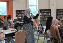 Kepala Perpustakaan UMS, Maria Husnun Nisa, berdiri memegang mikrofon saat mempresentasikan inovasi perpustakaan digital Program IMAM di hadapan akademisi University Malaya, Malaysia.