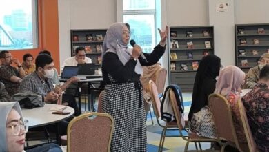 Kepala Perpustakaan UMS, Maria Husnun Nisa, berdiri memegang mikrofon saat mempresentasikan inovasi perpustakaan digital Program IMAM di hadapan akademisi University Malaya, Malaysia.