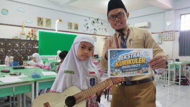Siswi memegang gitar ukulele dan guru menunjukkan poster promosi ekstrakurikuler SD Muhammadiyah 1 Solo di dalam ruang kelas.