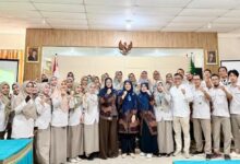 Sekelompok perawat RSI Purwokerto berhijab dan tim dosen Universitas Muhammadiyah Purwokerto (UMP) berpose bersama dengan pose tangan terkepal penuh semangat setelah sesi pelatihan penulisan artikel ilmiah. Latar belakang menunjukkan ruang Aula Diklat dengan lambang Garuda dan potret pemimpin negara.