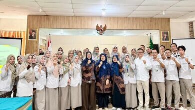 Sekelompok perawat RSI Purwokerto berhijab dan tim dosen Universitas Muhammadiyah Purwokerto (UMP) berpose bersama dengan pose tangan terkepal penuh semangat setelah sesi pelatihan penulisan artikel ilmiah. Latar belakang menunjukkan ruang Aula Diklat dengan lambang Garuda dan potret pemimpin negara.