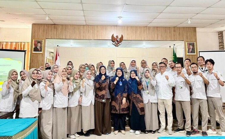 Sekelompok perawat RSI Purwokerto berhijab dan tim dosen Universitas Muhammadiyah Purwokerto (UMP) berpose bersama dengan pose tangan terkepal penuh semangat setelah sesi pelatihan penulisan artikel ilmiah. Latar belakang menunjukkan ruang Aula Diklat dengan lambang Garuda dan potret pemimpin negara.