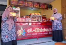 Dua pengelola berpose di depan gerai resmi El Chicken Pekalongan sambil memegang kemasan produk ayam andalan.
