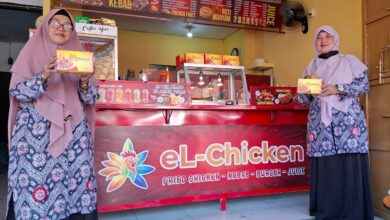 Dua pengelola berpose di depan gerai resmi El Chicken Pekalongan sambil memegang kemasan produk ayam andalan.