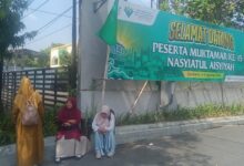 Tiga peserta wanita Muktamar Nasyiatul Aisyiyah Solo sedang beristirahat di pinggir jalan di depan spanduk ucapan selamat datang besar berwarna hijau. Spanduk tersebut memuat teks "Selamat Datang Peserta Muktamar ke-15 Nasyiatul Aisyiyah" dan tanggal acara di Surakarta, 6-8 Agustus 2026.