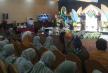 Penari tradisional dengan kostum hitam-emas tampil di atas panggung di hadapan ratusan anggota Nasyiatul Aisyiyah yang berkerudung seragam hijau muda di sebuah aula konvensi hotel saat acara formal, dengan latar belakang dekorasi panggung panel teal-emas dan bunga putih serta sebuah gong besar.