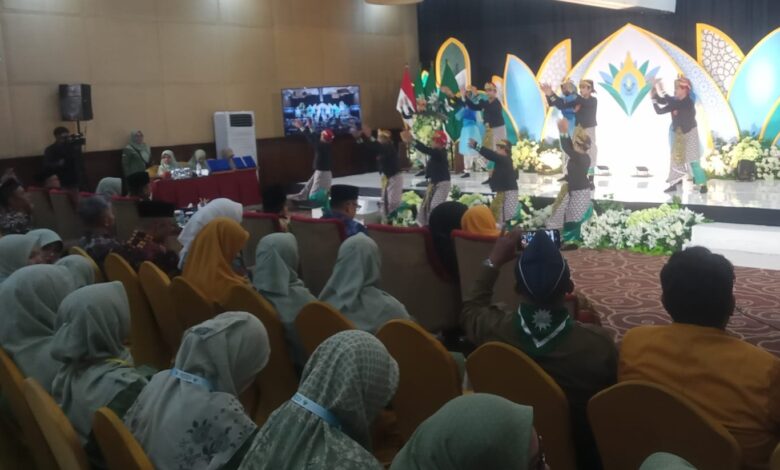 Penari tradisional dengan kostum hitam-emas tampil di atas panggung di hadapan ratusan anggota Nasyiatul Aisyiyah yang berkerudung seragam hijau muda di sebuah aula konvensi hotel saat acara formal, dengan latar belakang dekorasi panggung panel teal-emas dan bunga putih serta sebuah gong besar.