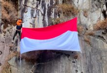 seorang pemanjat MALIMPA UMS sedang melakukan pengibaran bendera di tebing Wonosobo vertikal dengan peralatan lengkap dan bendera Merah Putih yang berkibar
