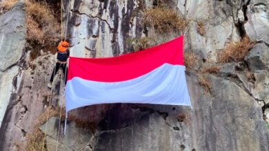 seorang pemanjat MALIMPA UMS sedang melakukan pengibaran bendera di tebing Wonosobo vertikal dengan peralatan lengkap dan bendera Merah Putih yang berkibar