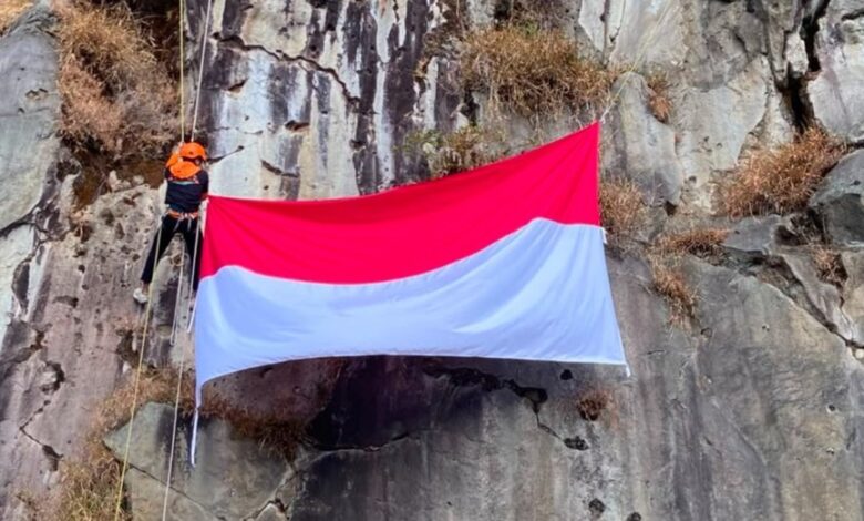 seorang pemanjat MALIMPA UMS sedang melakukan pengibaran bendera di tebing Wonosobo vertikal dengan peralatan lengkap dan bendera Merah Putih yang berkibar