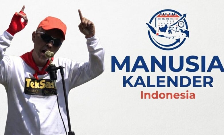 Zenza TekSas sang Manusia Kalender Indonesia tampil mengenakan topi oranye dan kacamata hitam sambil menunjuk ke atas di depan mikrofon.