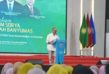 Bupati Banyumas, Sadewo Tri Lastiono, memberikan sambutan di podium UMP saat peluncuran PKBM Surya Muhammadiyah Banyumas, Ahad (9/8/2026). Di belakangnya terdapat layar besar acara dan tiga bendera panji.