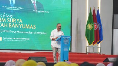 Bupati Banyumas, Sadewo Tri Lastiono, memberikan sambutan di podium UMP saat peluncuran PKBM Surya Muhammadiyah Banyumas, Ahad (9/8/2026). Di belakangnya terdapat layar besar acara dan tiga bendera panji.