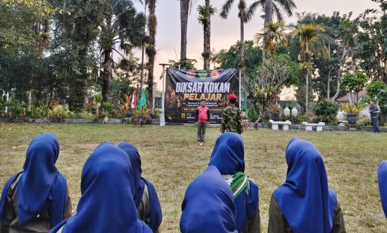 Suasana apel pembukaan Diksar KOKAM Pelajar Wonosobo dengan peserta berhijab biru berbaris rapi menghadap instruktur dan spanduk acara di area outdoor yang asri di The Lodjie Marong, Wonosobo.